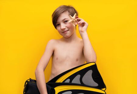 Tourist trip. Boy with fins for swimming, starfish on a yellow background. Travel insurance and reliability. Sea cruise with childrenの写真素材