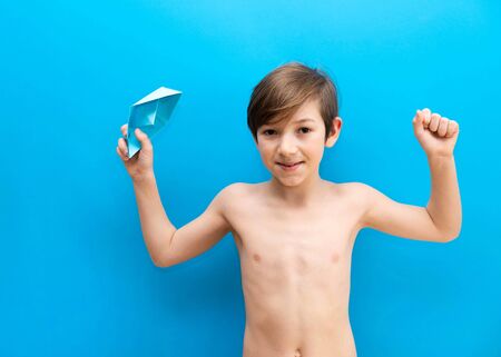 Boy with paper boats on a blue uniform background. The joy of the upcoming trip to the sea, sea cruise. Travel with babyの写真素材