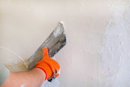 Stucco wall builder. Mens hands plaster the wall. Spatula in the hands of a male stator. Construction work in the house, paintingの写真素材