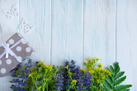 Summer wildflowers with gift box on a light wooden background with a place for inscription. Floral background for greeting card.の写真素材