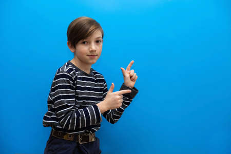 The boy points his fingers to the side. Photo of a cheerful boy on a blue background. Photo with a childの写真素材