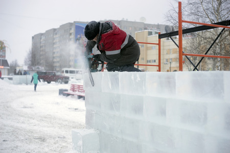 Man cuts electric saw ice wall in snow town.の写真素材