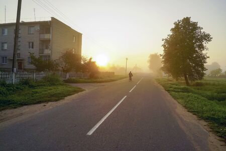 Morning fog with the rising sun on the street in the village .の写真素材