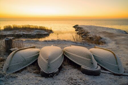 The first rays of the sun over lake Ladoga in the morning in winter. Overturned boats on a snowy beach. Leningrad region .の写真素材