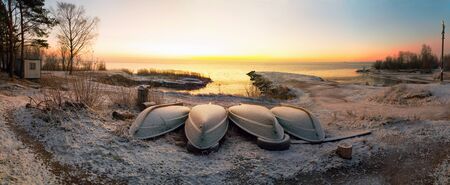 The first rays of the sun over lake Ladoga in the morning in winter. Overturned boats on a snowy...