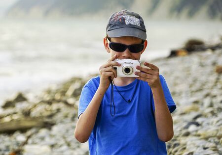 A boy with a camera shoots at the sea in the summerの写真素材