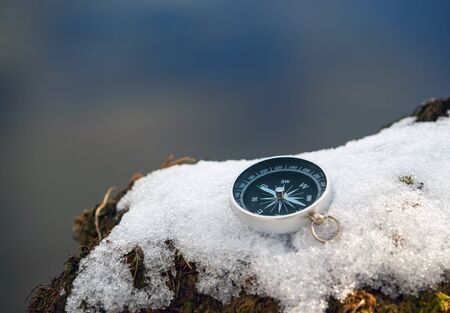 The compass is lying on the snow on the lake shore . The arrow points to the North