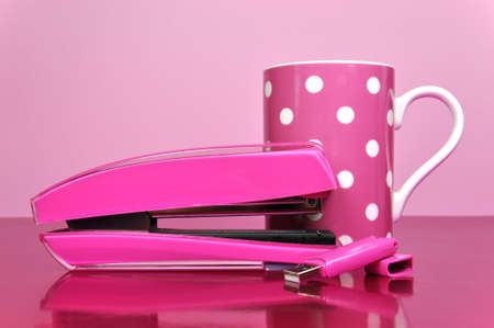 Pretty in Pink office accessories, stapler, pen drive, and polka dot mug, on a pink desk against a...