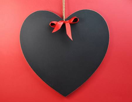 Heart shaped blackboard with red ribbon on a red background.の写真素材