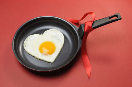 Red theme Valentine breakfast egg in fry pan with love on red background の写真素材
