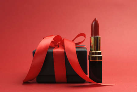 Beautiful luxury red lipstick with black box gift against a red background の写真素材
