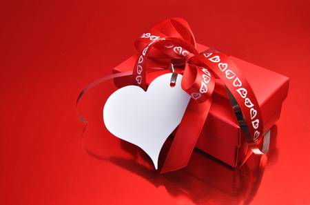 Red present gift with white heart shaped gift tag and ribbons and bow on a red background, for Valentine or saying, I Love You の写真素材