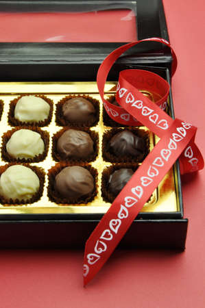 Beautiful Valentine black and gold box of delicious white, milk and dark chocolates in a black and gold box with romantic red heart ribbon on a red background の写真素材