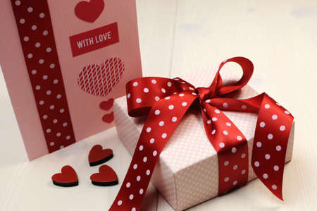 Handmade gift card with pink gift and red polka dot ribbon and heart on white natural wood table の写真素材