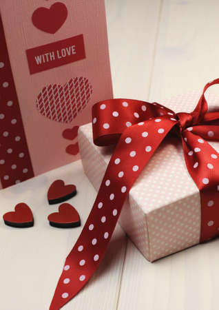 Handmade gift card with pink gift and red polka dot ribbon and heart on white natural wood table の写真素材