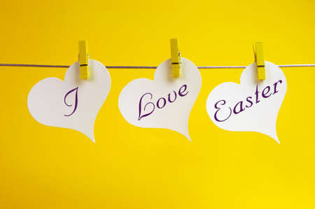 I Love Easter message written acorss 3 heart tags hanging from pegs on line against a yellow...