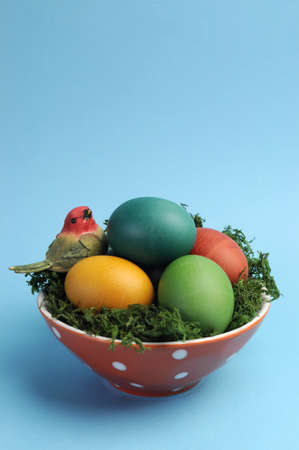 Bright and cheerful Happy Easter still life with rainbow color eggs in orange polka dot bowl against a blue background, with red robin bird - vertical with copy space の写真素材
