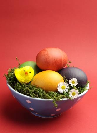 Bright and cheerful Happy Easter still life with rainbow color eggs in blue polka dot bowl against a red background - vertical with copy space の写真素材