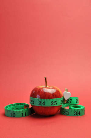 Weight loss slimming diet concept, New Year Resolution, with green measuring tape around a bright red apple, set against a red background  vertical with copy space の写真素材