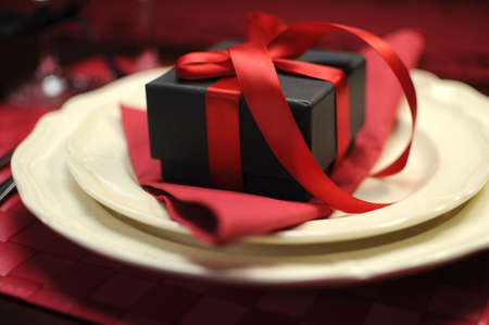Closeup with bokeh of black box present gift with red ribbon on romantic Valentine table setting の写真素材