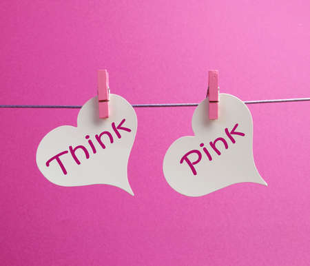  Think Pink  message written on two white hearts hanging from pink pegs against a pink background の写真素材