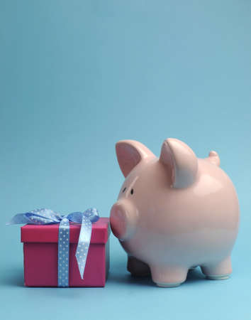 Pink Piggy Bank with pretty pink gift and blue polka dot ribbon bow against a blue background, vertical with copy space for your text here の写真素材