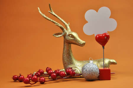 A gold glitter reindeer Christmas ornament with red berries and silver ornament against a gold...
