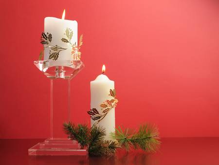 Lit white Christmas candles with festive holiday gold decoration and pine branches decorations against a festive holiday red background の写真素材