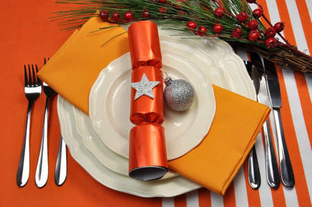 Bright and colorful orange theme Christmas table setting with plates, forks and knives, Christmas Bon Bons Crackers with decorations for a lively, stylish and fun holiday party atmosphere の写真素材