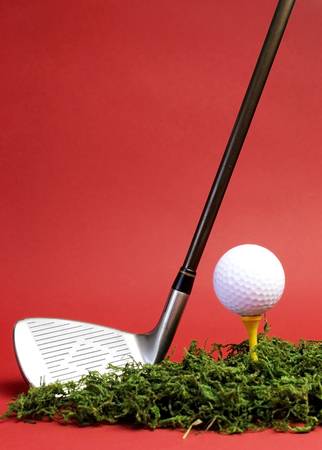 Sporting and Leisure pursuit, golf club iron, yellow tee with white golf ball on grass against  a red background, vertical with copy space.の写真素材