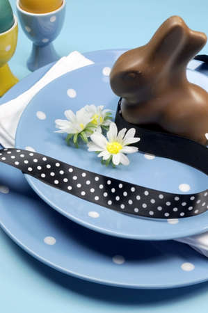 Happy Easter dinner table setting with blue polka dot plates, and decorations against a blue background  Vertical close-up with chocolate Easter bunny rabbit の写真素材