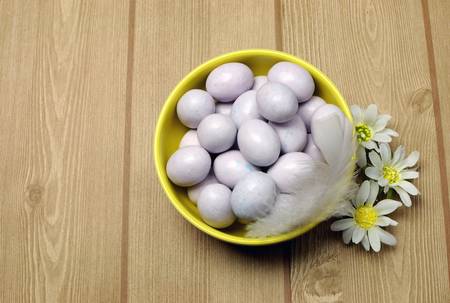 Yellow bowl of sugar candy mini Easter eggs on a natural timber table background.の写真素材