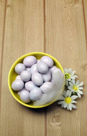 Yellow bowl of sugar candy mini Easter eggs on a natural timber table background. Vertical with copy space.の写真素材