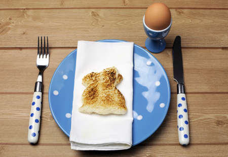 Breakfast dinner table setting with Easter bunny rabbit toast and egg with blue polka dot on natural timber wood table.の写真素材