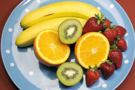 Platter of fruit - bananas, orange, kiwi fruit and strawberries - on blue polka dot platter for healthy diet and fitness の写真素材