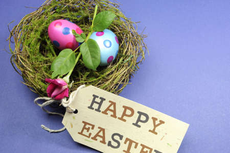 Pink and blue polka dot eggs with rose bud in nest with Happy Easter gift tag の写真素材