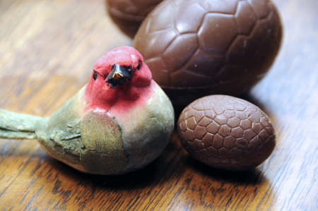 Closeup of small red robin bird with chocolate Easter eggs on a wood table background の写真素材