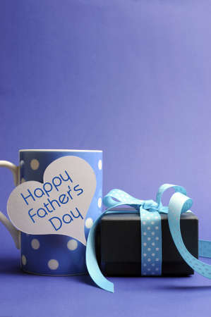 Happy Fathers Day message written on white heart gift tag on blue polka dot mug with black box gift...