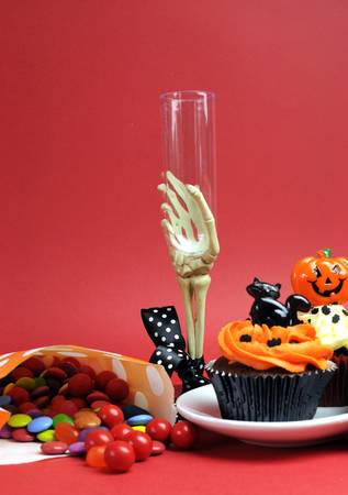 Happy Halloween party food with skeleton hand glass on red background, with cupcakes and candy lollies. Vertical with copy space.の写真素材