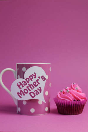 Happy Mothers Day message on white heart tag with pink polka dot coffee mug and pink cupcake -...
