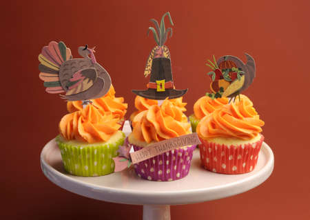 Happy Thanksgiving decorated cupcakes with turkey, pilgrim hat and corn toppers on cake stand against a brown background.の写真素材