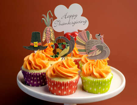 Happy Thanksgiving decorated cupcakes with turkey, pilgrim hat and corn toppers on cake stand against a brown background, with Happy Thanksgiving message.の写真素材
