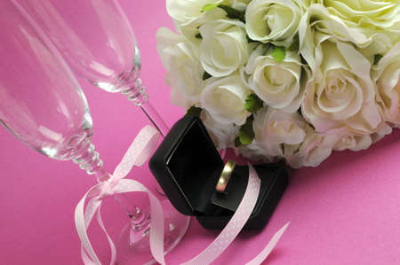 Wedding bridal bouquet of white roses on pink background with pair of champagne flute glasses and wold weggind ring in black jewellery box.の写真素材