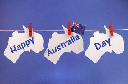 Celebrate Australia Day holiday on January 26 with a Happy Australia Day message greeting written across white Australian maps and flag hanging pegs on a line against a blue background の写真素材