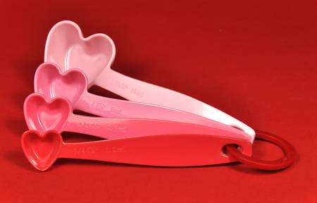 Love theme pink and red heart shape measuring spoons against a red background for Valentine, birthdya, Christmas, Mothers Day or romantic baking and cooking の写真素材