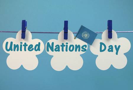 United Nations Day greeting message written across white tags with flag hanging from blue pegs on a line against a sky blue background for the October 24 celebration の写真素材