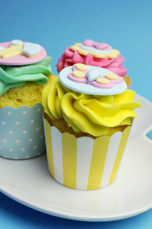 Beautiful pink, aqua blue and yellow cupcakes on white heart shape plate, for baby shower or...
