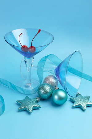 Festive spirit blue martini cocktai glasses with red maraschino cherries and christmas baubles on an aqua blue background. Vertical.の写真素材