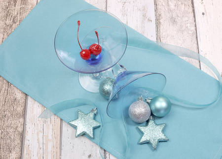Festive spirit blue martini cocktai glasses with red maraschino cherries and christmas baubles on a shabby chic tableの写真素材