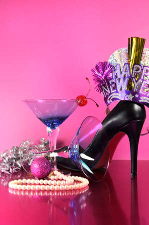 Pink theme Happy New Year party with vintage blue martini cocktail glass and New Years eve decorations against a pink background, with female high heel shoe, pearls and festive ornaments  Vertical の写真素材
